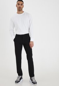 Črne krojene hlače, slim fit z gladko teksturo, v kombinaciji z belim dolgimi rokavi. Teniske imajo sivo in mornarsko modre detajle.