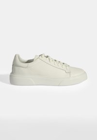 White leather sneaker with textured side panels, flat laces, and a thick rubber sole. Rounded toe and minimalistic design.