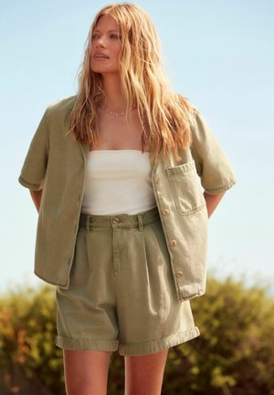Chemise en lin vert clair à manches courtes, assortie à un short plissé. La tenue comprend un top bandeau blanc en dessous.