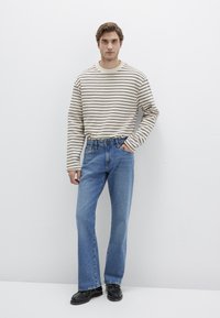 Striped beige and brown long-sleeve shirt paired with blue denim jeans and black shoes, standing against a plain white background.
