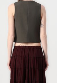 Krótk top bez rękawów w ciemnym oliwkowym kolorze, charakteryzujący się prostym krojem z prostym dołem i minimalnymi szwami, w połączeniu z warstwową bordową spódnicą.