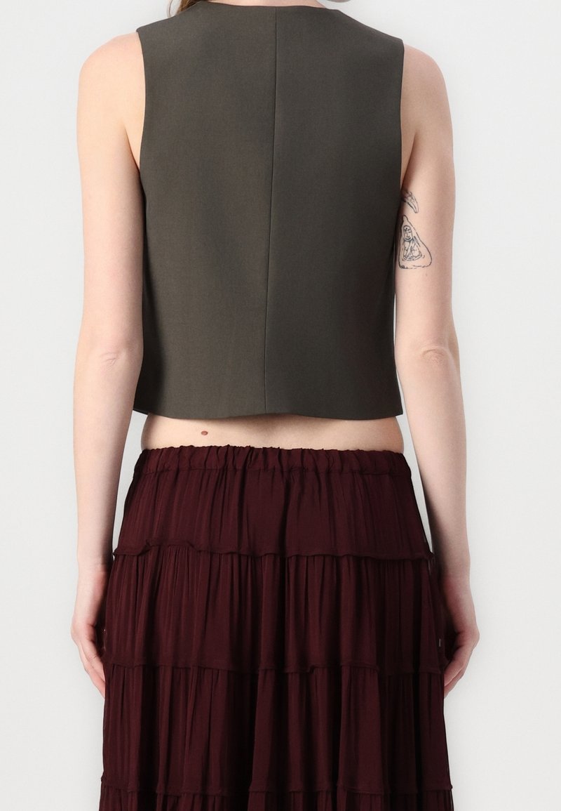 Krótk top bez rękawów w ciemnym oliwkowym kolorze, charakteryzujący się prostym krojem z prostym dołem i minimalnymi szwami, w połączeniu z warstwową bordową spódnicą.
