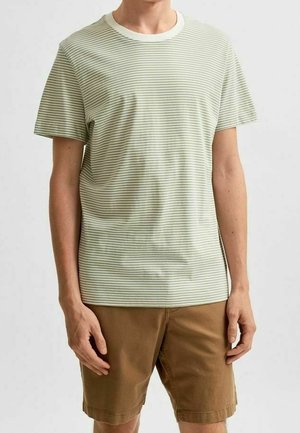 Vihreä-valko raidallinen lyhythihainen t-paita, jossa kontrastivärinen valkoinen pyöreä pääntie, yhdistetty ruskeisiin shortseihin. Pehmeä kangas, rento istuvuus.