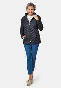 Doudoune navy avec motif en chevrons, fermeture éclair sur le devant et deux poches latérales. Associée à un jean bleu et des baskets de couleur claire.