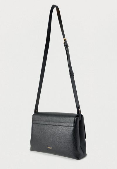 Μαύρο δερμάτινο τσαντάκι χιαστί με υφή, ρυθμιζόμενο λουρί, μαγνητικό κλείσιμο με καπάκι και χρυσή λεπτομέρεια με λογότυπο στο μπροστινό μέρος.