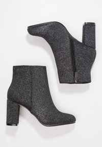 Svarta glittriga ankelstövlar med klack. Har en sidodragkedja för stängning. Slen yta med en glänsande finish. Högklackad design.