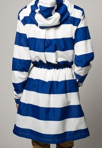 Blå och vit randig regnjacka med huva, elastisk midja och en blank, slät yta, som når till mitten av låret.