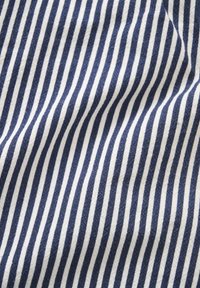 Blauw-wit gestreept stof met verticale strepen, zichtbare textuur en lichte plooien die zachte schaduwen creëren.