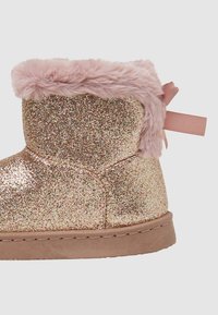 Stivaletto rosa glitterato realizzato in materiale lucido, con un ampio risvolto in pelliccia sintetica rosa e un nastro decorativo sul retro. Sole piatto.