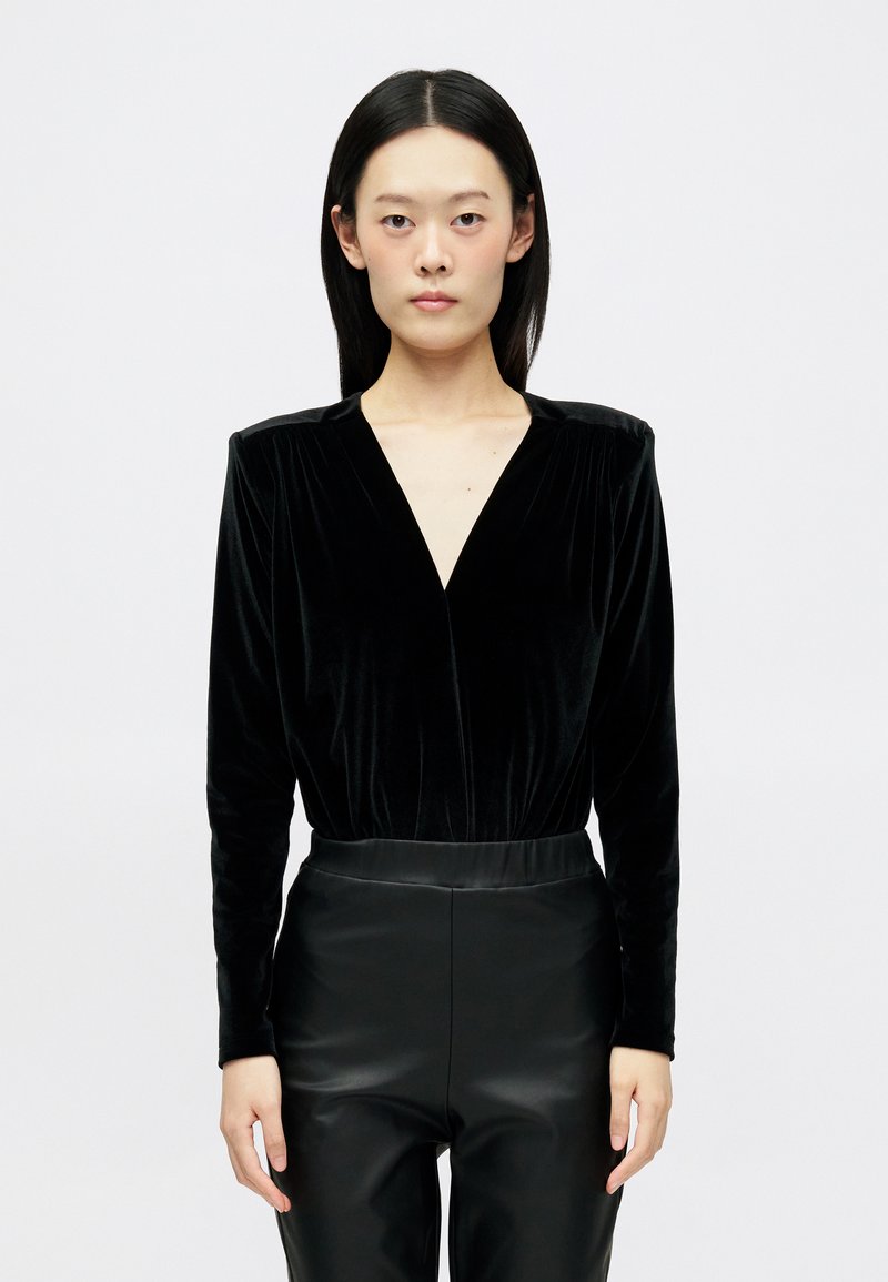 Body din catifea neagră, cu mâneci lungi și decolteu adânc în V, cu pliseuri la umeri și talie ajustată. Asortat cu pantaloni din piele neagră, eleganți.