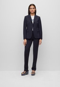 Completo blu navy con blazer adattato e pantaloni, dotato di spalle strutturate e patte. Abbinato a scarpe platform a fantasia.