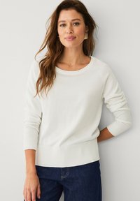 Maglione bianco lavorato a maglia con scollatura rotonda, polsini a coste e una vestibilità leggermente cropped, abbinato a jeans in denim blu scuro.