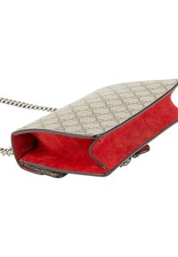 Petit sac bandoulière de créateur avec extérieur beige à motif et intérieur en daim rouge vif, doté d'une fine chaîne argentée en bandoulière.