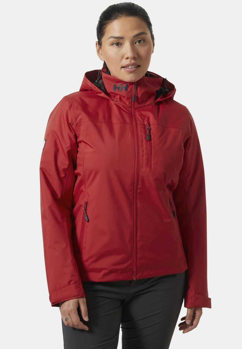 Czerwona wodoodporna kurtka z kapturem, zamykanymi kieszeniami i gładką teksturą. Szczegół z logotypem na kołnierzu dodaje widocznego brandingu.