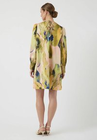 Bloemenpatronen jurk van zachte, lichte stof. Heeft lange mouwen en een sleutelgatrug met strikjes. Kleuren omvatten pastelroze, groen en blauw.