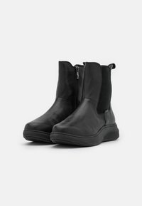 Botines de cuero negro hasta el tobillo con paneles laterales elásticos y cierre de cremallera. Diseño estructurado con punta redonda y suela de goma texturada.