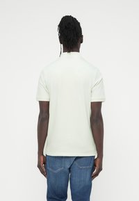 Ανοιχτό πράσινο πό λο μπλουζάκι από βαμβάκι, με κοντά μανίκια και κανονικό γιακά. Φορεμένο με μπλε τζιν παντελόνι.