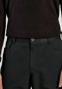 Black trousers with a smooth texture, featuring side pockets, a button closure, and a fitted design. Worn with a dark sweater.