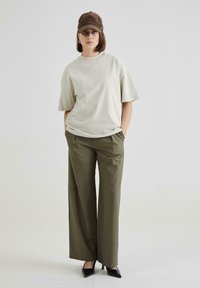 Oversized cream t-shirt, olive wide-leg trousers, and black high-heeled shoes. Brown cap with embroidered detail.