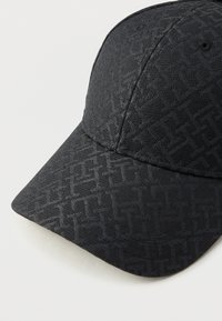 Μαύρο καπέλο μπέιζμπολ με μια διακριτική υφή γεωμετρικού μοτίβου που καλύπτει το ύφασμα, παρουσιασμένο σε ανοιχτό φόντο.