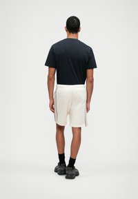 Zwarte T-shirt met korte mouwen, gecombineerd met crèmekleurige shorts met zijaccenten, elastische tailleband en zwarte sneakers met een gestructureerde zool.