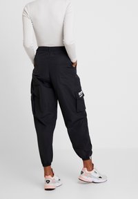 Svarta cargobyxor med två sidofickor och elastiska muddar, tillverkade av ett lätt material. Bärs tillsammans med vita och rosa sneakers.