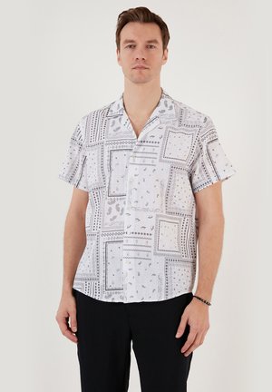 Rövid ujjú ing fehér anyagból, fekete geometriai és virágmintákkal, laza fazonnal és nyitott gallérdizájnnal.