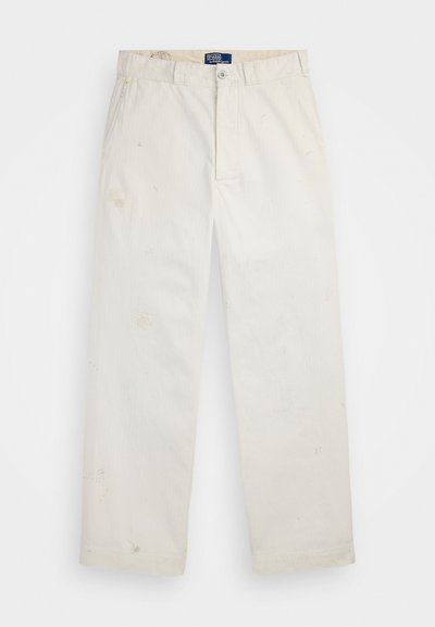 Bijele pamučne hlače s dizajnom ravnog kroja, vidljivim mrljama i zatvaranjem na dugme. Sadrže prednje džepove i oznaku na pojasu.