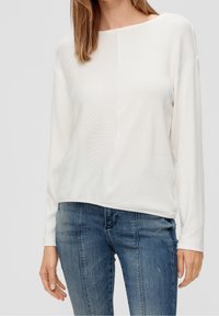 Wit top met lange mouwen en een losse pasvorm, met een subtiel gestructureerd ontwerp en een afgeronde halslijn, gecombineerd met blauwe slim-fit jeans.