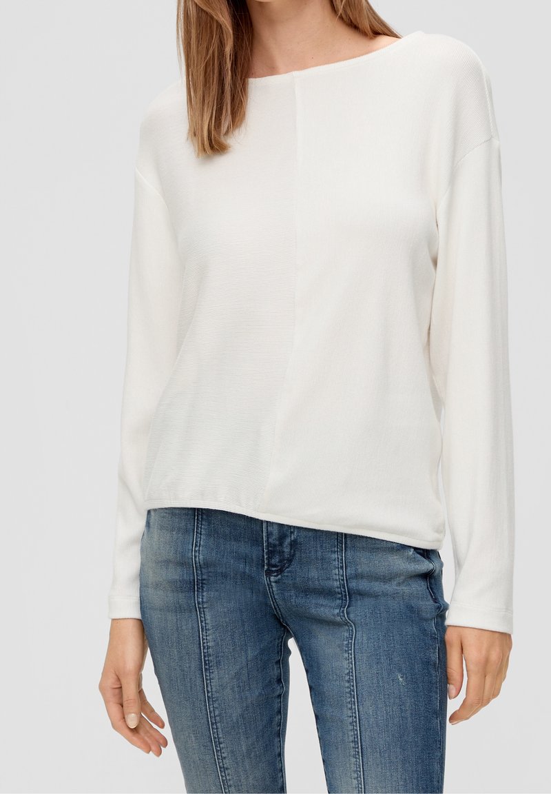 Wit top met lange mouwen en een losse pasvorm, met een subtiel gestructureerd ontwerp en een afgeronde halslijn, gecombineerd met blauwe slim-fit jeans.