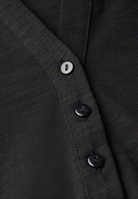 Tissu tricoté noir avec patte de boutonnage comportant un bouton blanc et deux boutons ronds noirs, vue en gros plan de la texture et des coutures.