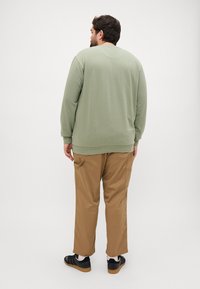 Olijfgroene sweatshirt met lange mouwen, ronde hals en geribbelde manchetten, gecombineerd met tan cargobroek en zwarte sneakers.