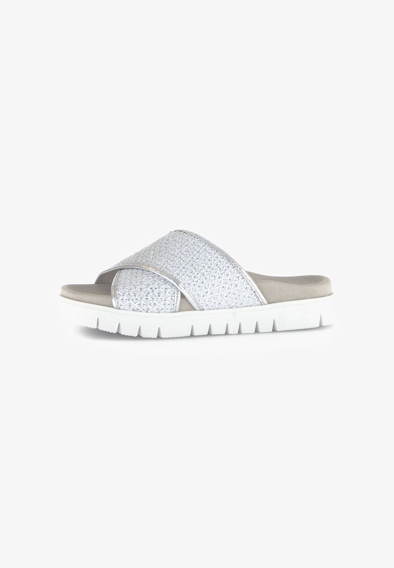 White slide sandals feature crisscross woven upper, soft beige footbed, and a thick white outsole with a ridged pattern for traction.