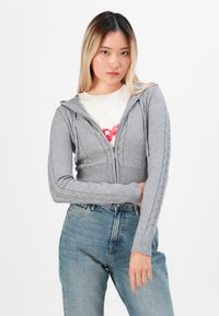 Grijze cropped hoodie met een rits, voorzien van kabelgebreide accenten op de mouwen en een ribgebreide zoom. Gecombineerd met high-waisted blauwe jeans.