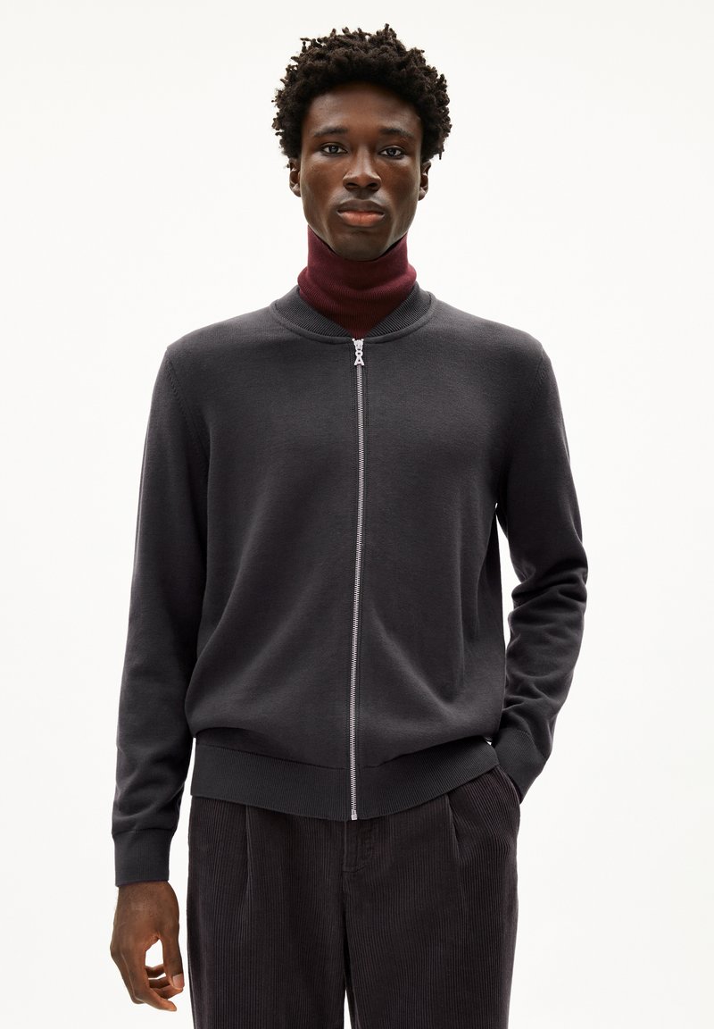 Dunkelgrauer Reißverschluss-Pullover aus einem weichen Material, mit einem runden Kragen und gerippten Bündchen. Getragen über einem weinroten hochgeschlossenen Oberteil.