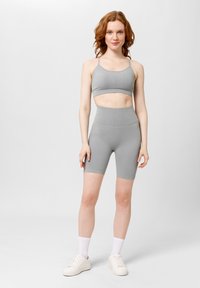 Šedý sportovní podprsenka a set vysoko-licheraných šortek. Obsahuje ribbovanou strukturu, pohodlný tvar a tenké ramínka. Nosené s bílými teniskami a ponožkami.