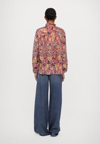 Blomstret bluse med volangkrage i rosa, rød og gultoner, parret med vide denimbukser. Mønsteret har intrikate design.