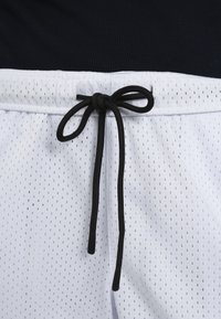 Shorts en mesh blanc avec une taille élastique noire et un cordon noir noué en nœud devant au centre.