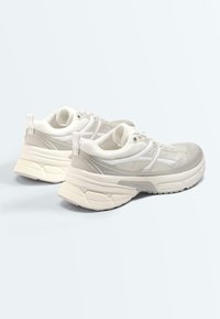 Paire de baskets épaisses blanches et grises avec semelles épaisses, tiges en mesh et cuir, et fermetures à lacets sur un fond uni clair.