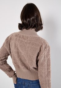 Suéter texturado beige con un alto cuello acanalado, patrón de diamantes y bajo acanalado ajustado. La tela parece suave y esponjosa.