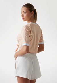 Persiko-färgad cropped t-shirt med vit kantning och korta ärmar, kombinerad med vita shorts med elastisk midja, som visar en avslappnad passform och mjuk textur.