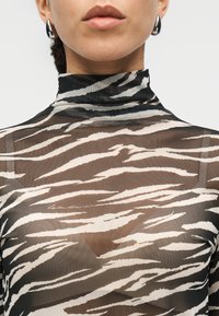 Διάφανο μαύρο τοπ με ψηλό γιακά, διακοσμημένο με μοτίβο ριγέ ζέβρας σε μαύρο και μπεζ. Μαλακή υφή με αξιοσημείωτες λεπτομέρειες σχεδίου.