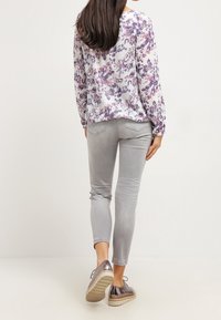 Blusa de manga larga con estampado floral en blanco con tonos púrpura y rosa, combinada con jeans ajustados grises claros y zapatos plateados brillantes.