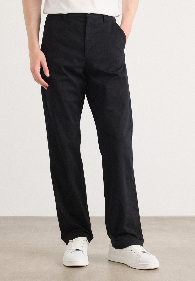 Black trousers featuring a straight-leg design, made from smooth fabric, with a classic waistband and side pockets, paired with white sneakers.