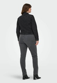 Svart denimjacka med en figursydd design, enkel bak och knäppningar vid handlederna, matchad med grå figursydda jeans och svarta ankelboots.