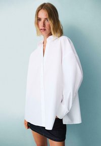 Camicia bianca oversize con colletto a camicia, maniche lunghe e orlo dritto, abbinata a una minigonna in denim scuro.
