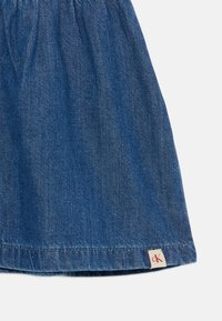 Traper suknja u tamnoplavoj boji, s naboranom teksturom i obrubljenim rubom. Mala oznaka s "CK" vidljiva je blizu dna.