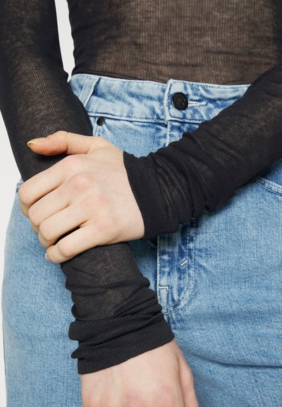 Black ribbed long-sleeve top with gathered cuffs, worn over blue high-waisted denim jeans. The fabric appears sheer and textured.