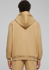 Hanorac cu glugă de culoare khaki, fabricat dintr-un material moale, cu un croi lejer, manșete ribbate și o glugă confortabilă. Textură fină, design minimalist.