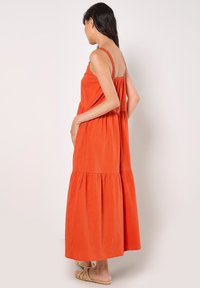 Oranje gelaagde maxi-jurk van lichtgewicht stof met verstelbare bandjes en geplooide rugdetails. Draag met beige sandalen.